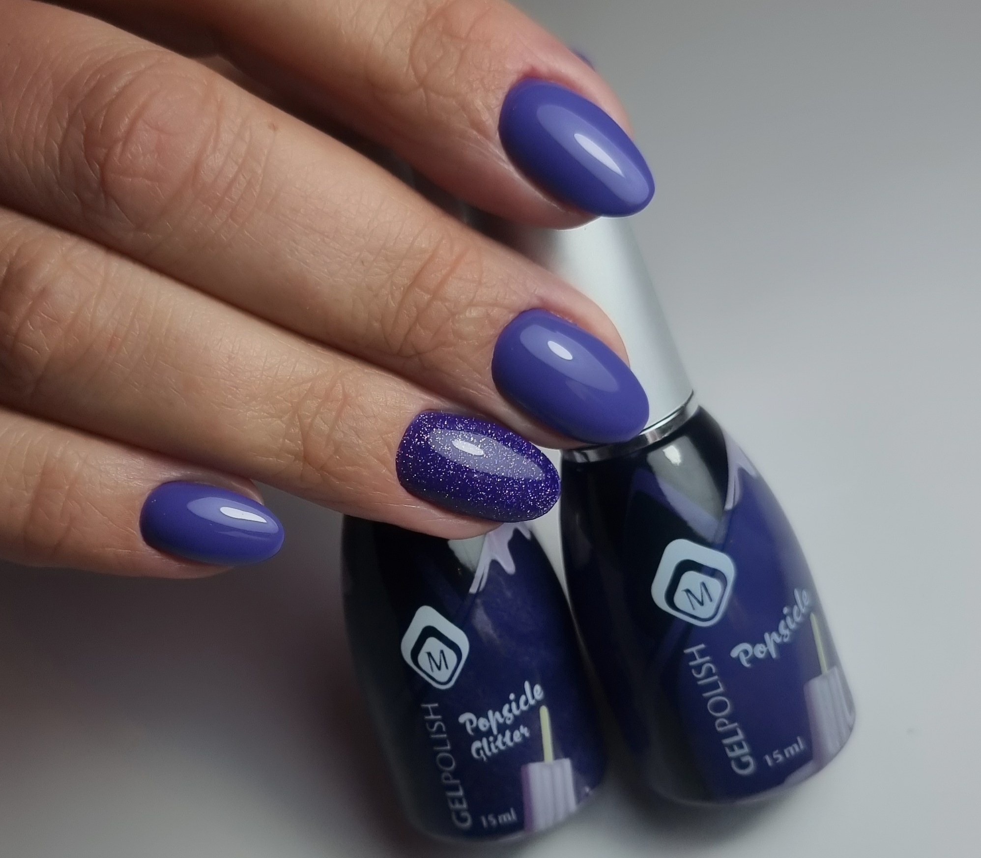 Violette nagels naast twee flesjes gellak met glitter